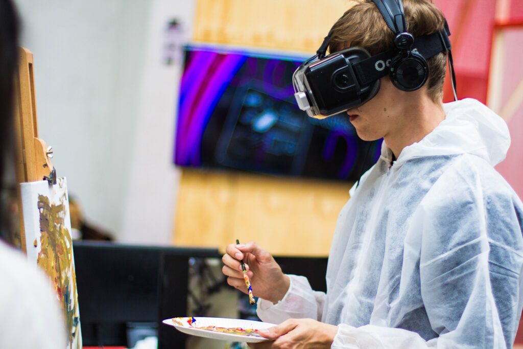 A photo of an artist with virtual reality (VR) goggles paints from a palette to a canvas.