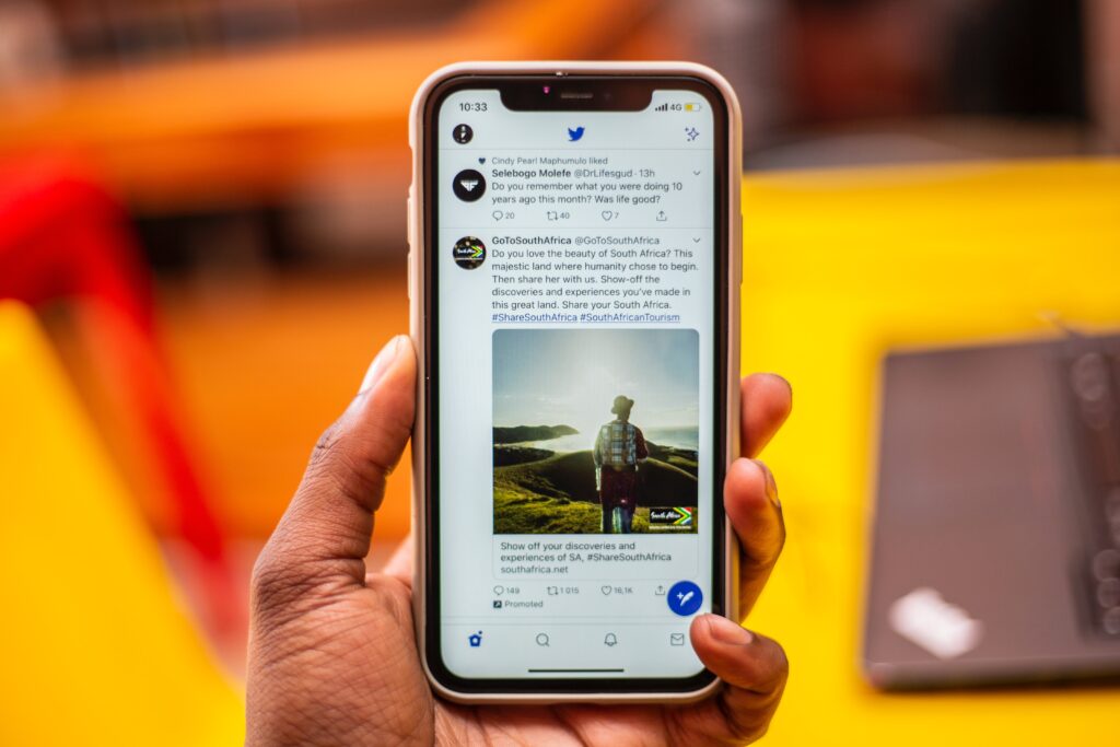 A photo of a hand holding a smartphone displaying text and photos from Twitter in front of a yellow, red and gray background.
