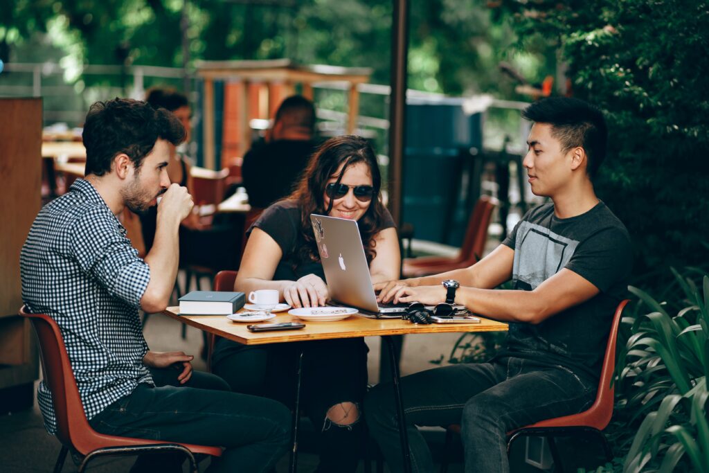 Photo of Three people on a cafe patio search for content on a laptop computer.