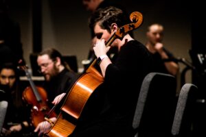 A photo of a cellist with smartwatch and the orchestra in the background.